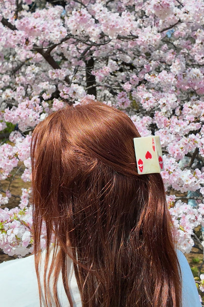 Person with a hair clip featuring ace of hearts against a cherry blossom background