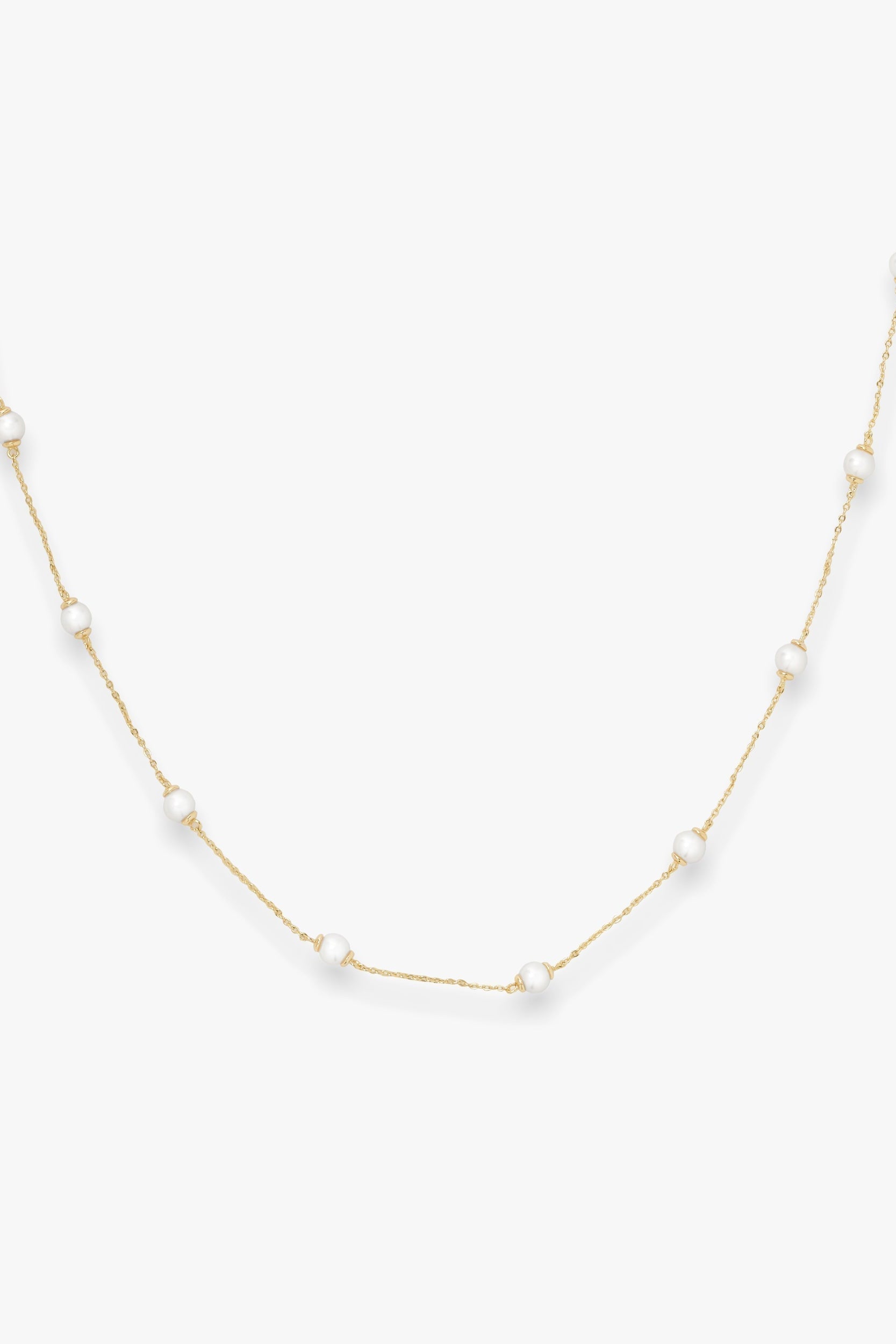 Gold infinity necklace with pearls on a white background