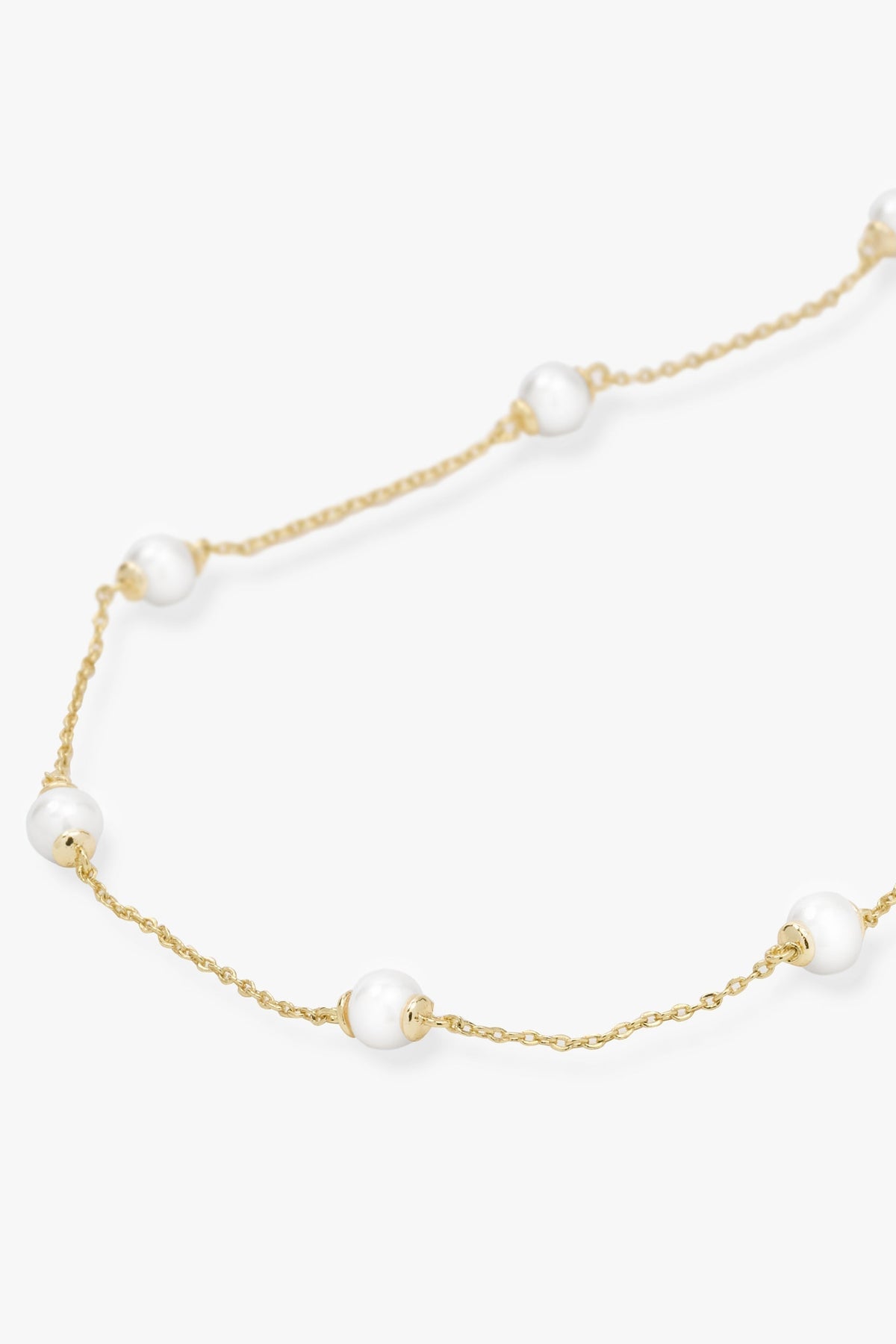 A delicate gold chain necklace featuring evenly spaced, small white pearl beads, displayed on a clean off-white background.