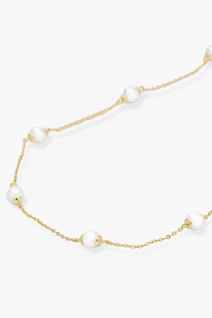 A delicate gold chain necklace featuring evenly spaced, small white pearl beads, displayed on a clean off-white background.