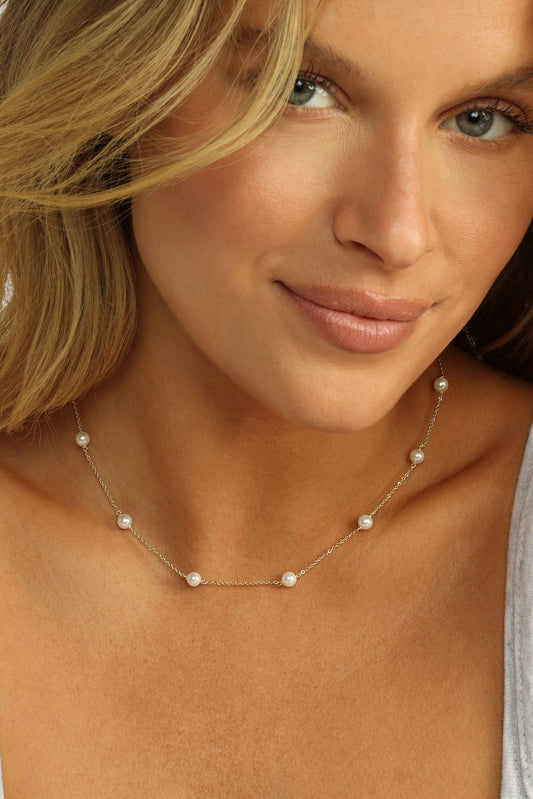 Woman wearing a pearl infinity necklace against a white background