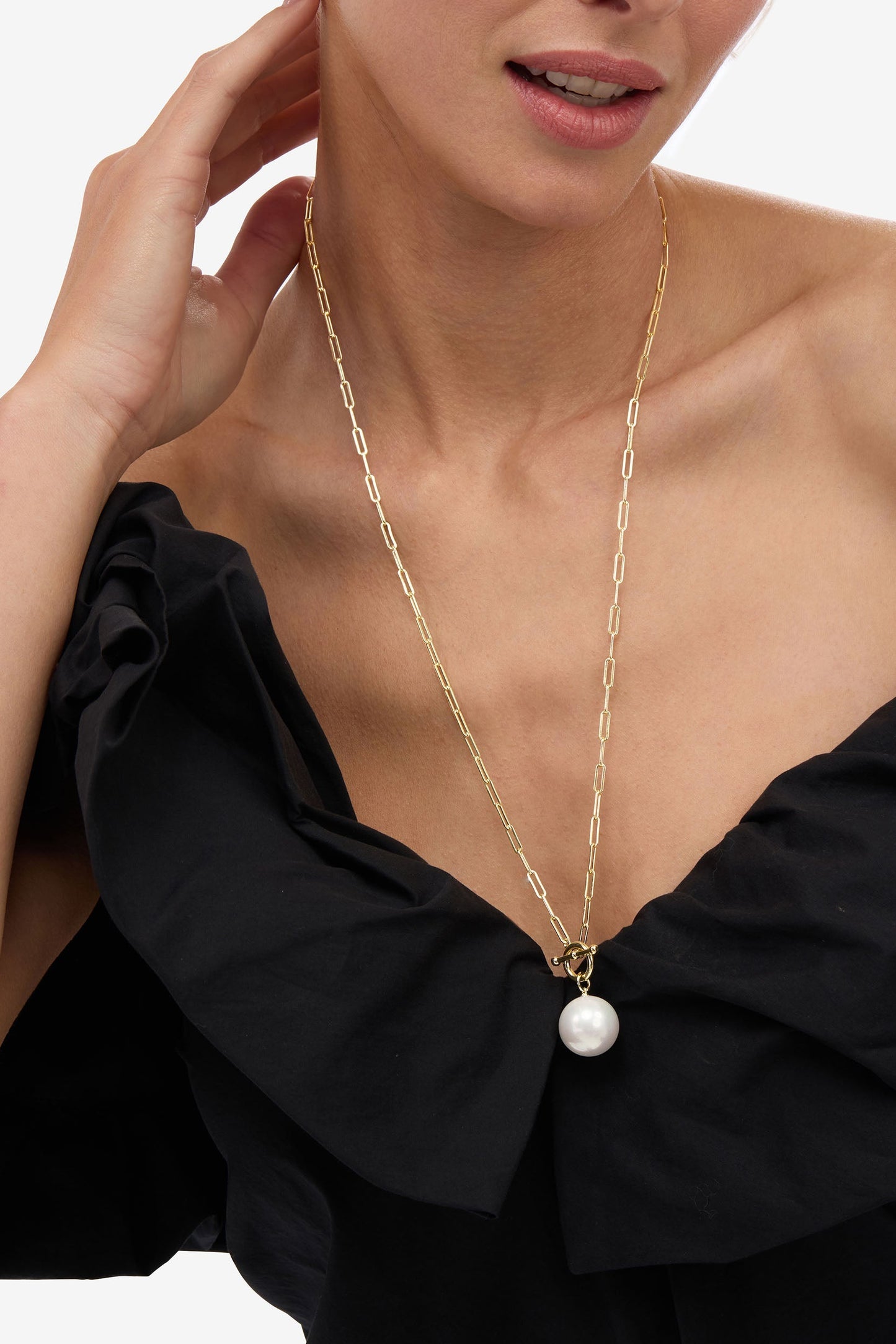 Woman wearing a gold necklace with a large pearl pendant on a plain background