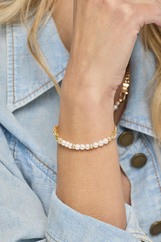 A close-up of a woman's wrist wearing a delicate gold bracelet with white pearl beads, styled with a light blue denim jacket.