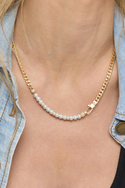 A close-up of a model wearing a delicate gold chain necklace with a single strand of small white pearls and a gold clasp, styled with a light blue denim shirt.