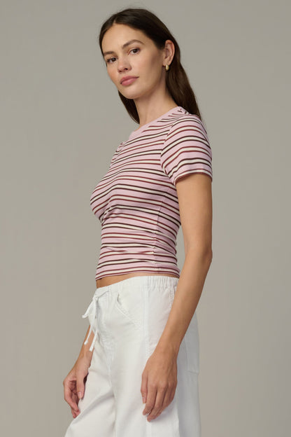 Woman wearing a blush/ecru striped shirt and white pants against a neutral background