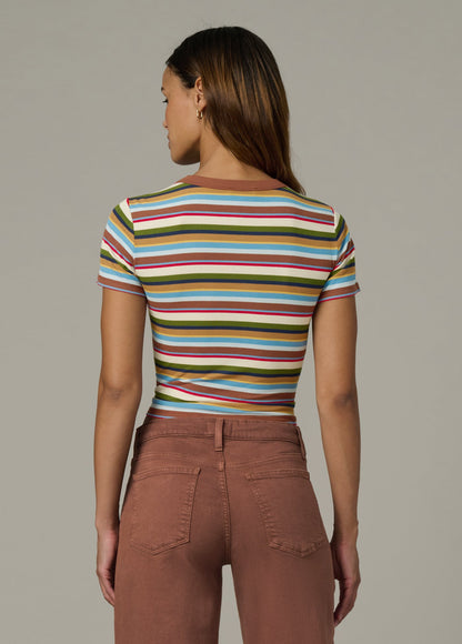 Back view of woman wearing a baby tee in multi variegated stripes with brown pants against a neutral background