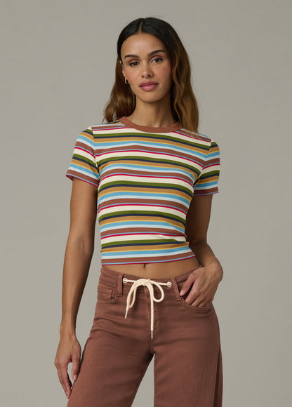 Woman wearing a baby tee in multi variegated stripes with brown pants against a neutral background