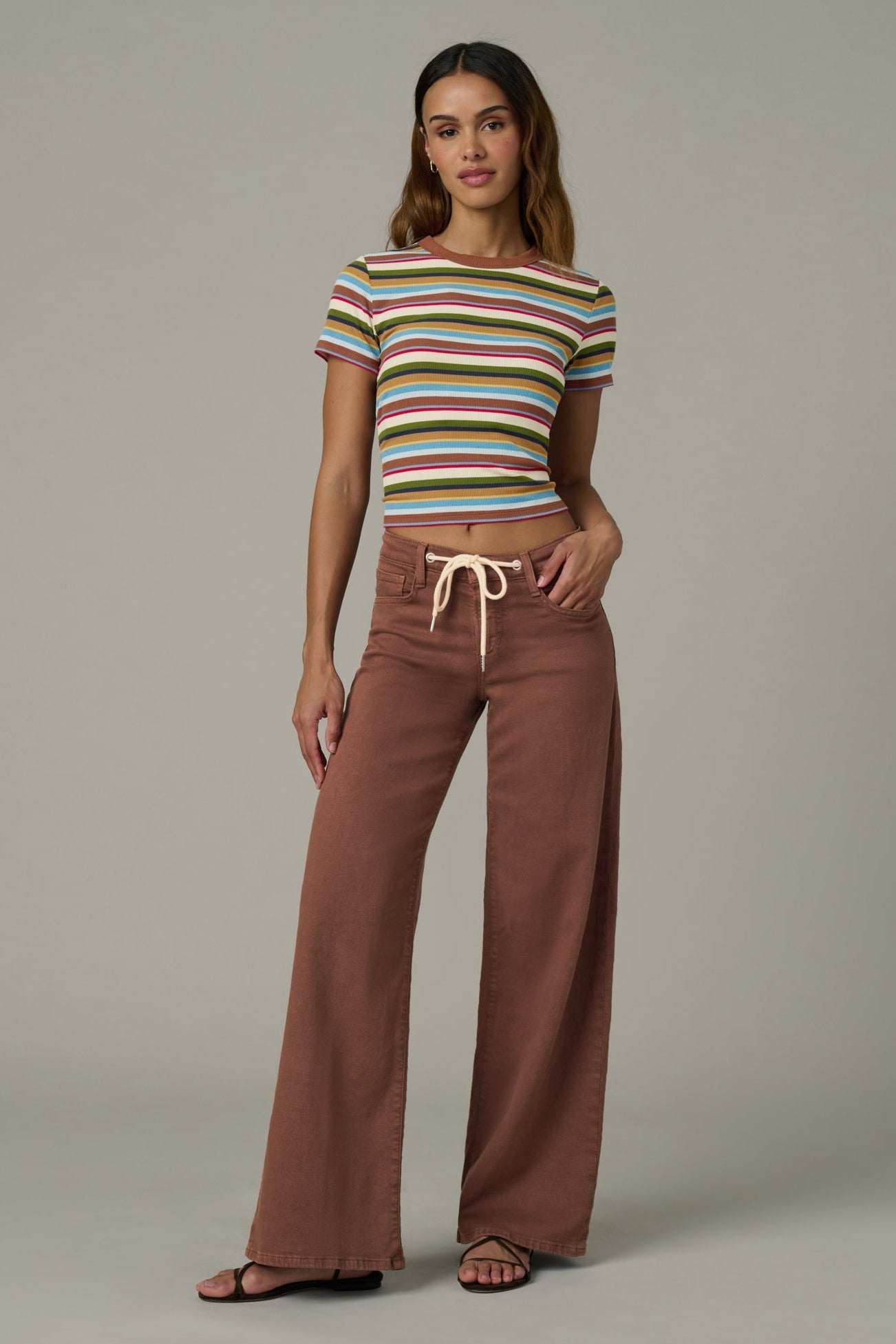 Woman wearing a striped crop top and chocolate color Lou Lou wide-leg pants  with a drawstring on a plain background