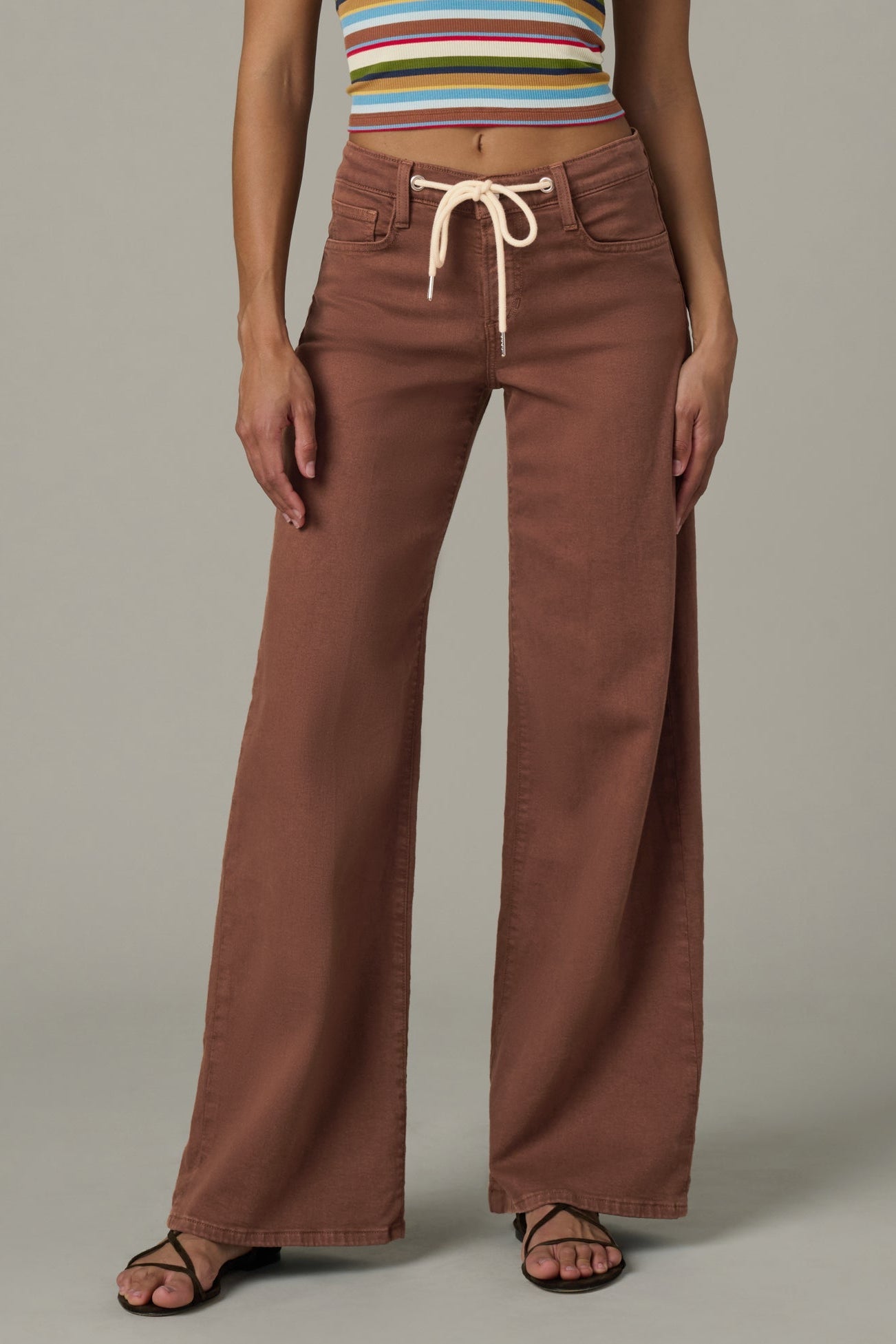 Woman wearing a striped crop top and chocolate color Lou Lou wide-leg pants  with a drawstring on a plain background