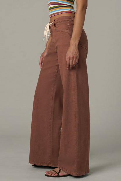 Side view of woman wearing a striped crop top and chocolate color Lou Lou wide-leg pants  with a drawstring on a plain background