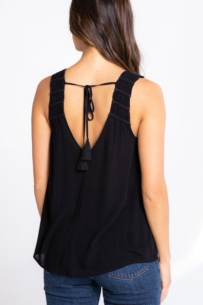 Black sleeveless top with open back and tassel details worn by a person on a white background