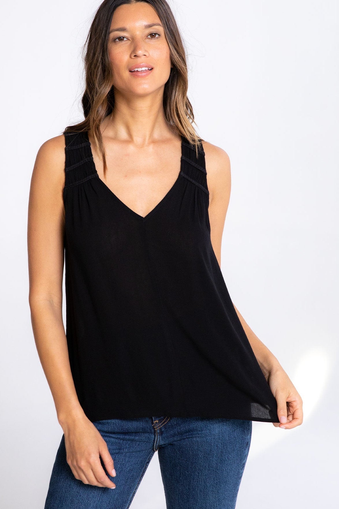 Woman wearing a black sleeveless vneck top and blue jeans on a white background