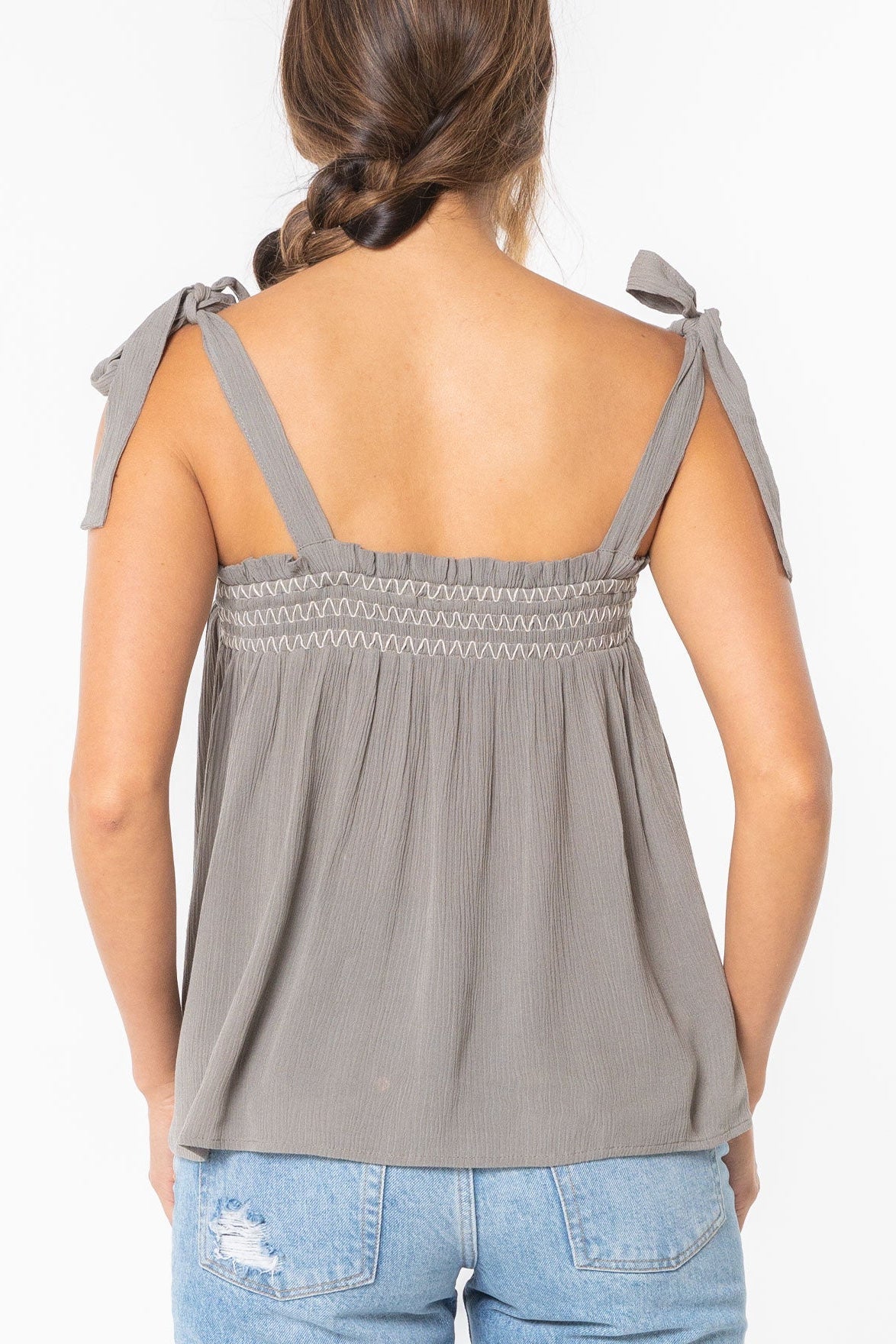 Woman wearing a cement gray sleeveless top with bow straps on a white background