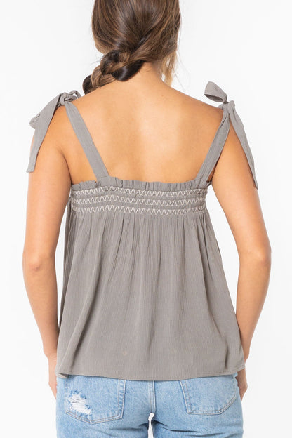 Woman wearing a cement gray sleeveless top with bow straps on a white background