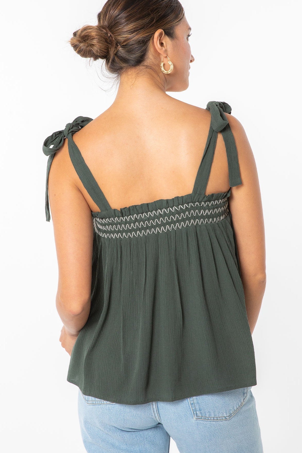 Woman wearing a military green top with bow straps on a white background