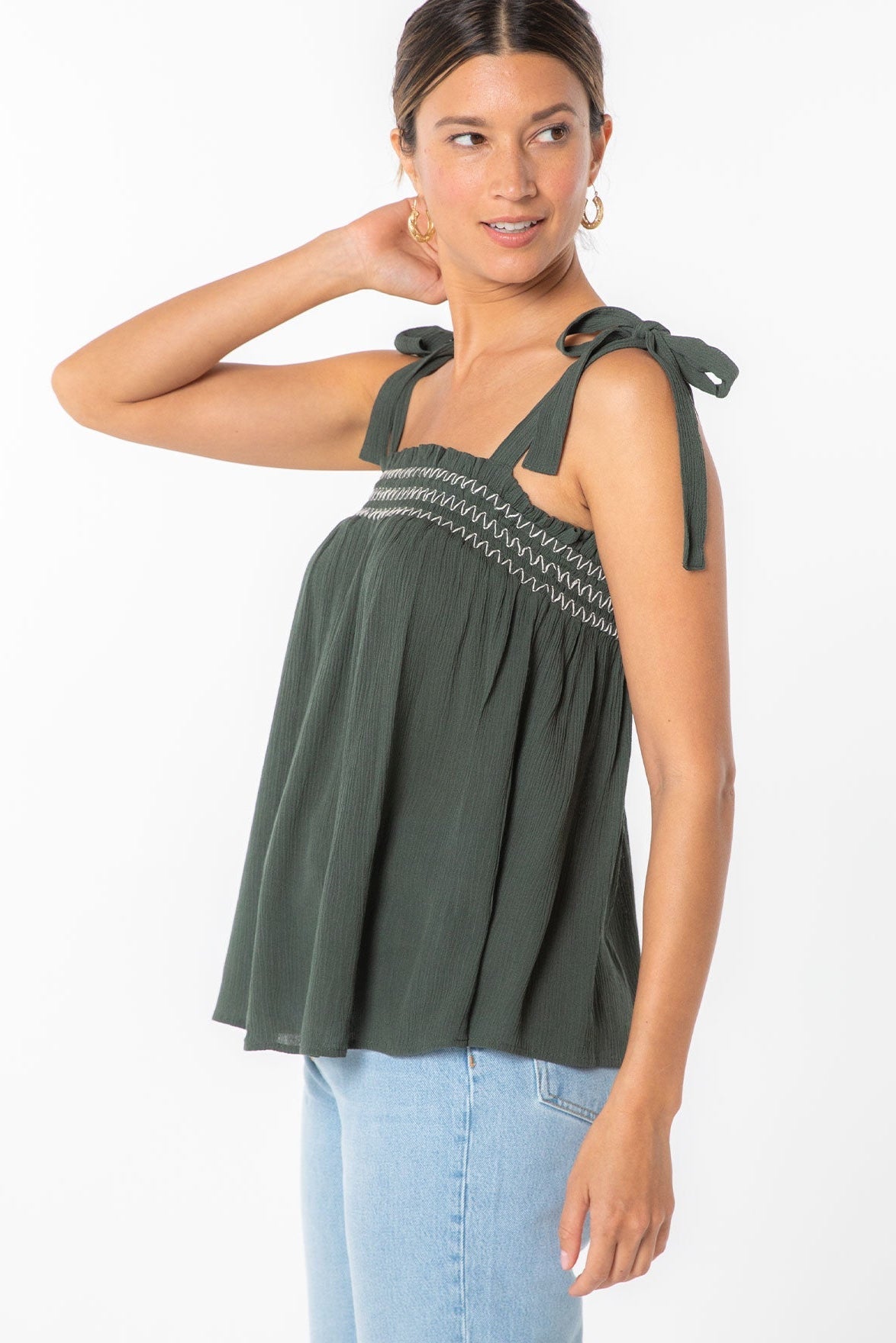 Woman wearing a military green sleeveless top with bow straps on a white background