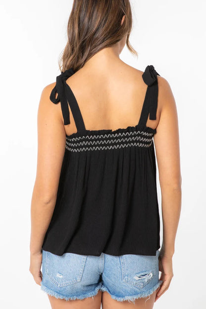 Black smocked tank top with zigzag trim and tie bow shoulder straps, back view