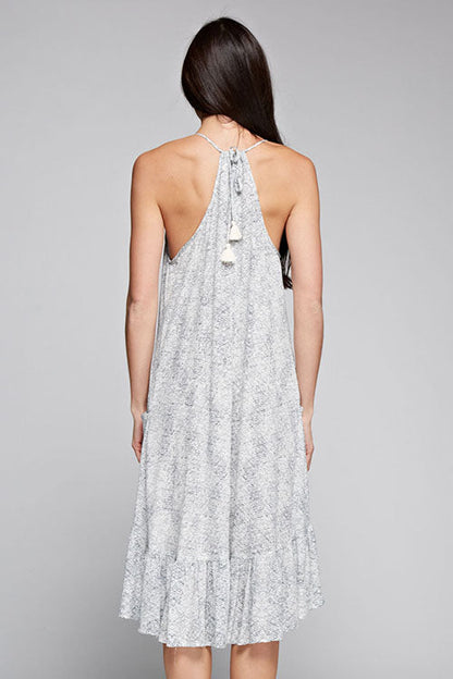 A woman viewed from the back wearing the kangaroo hi low midi dress with a light gray and white abstract print and tassel tie at the neckline, set against a solid gray studio background.
