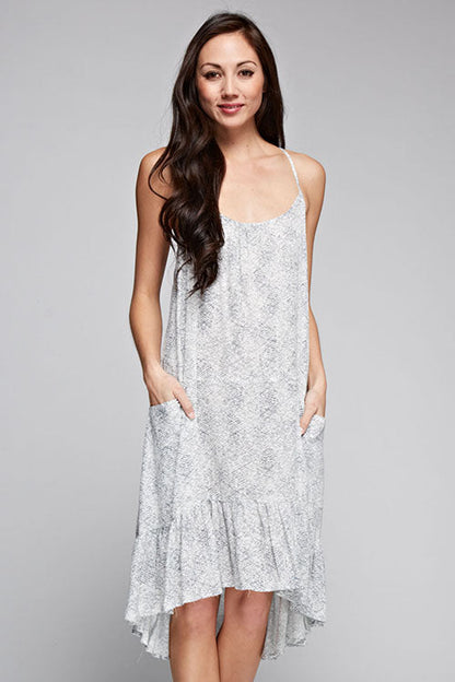 A woman modeling a light gray and white patterned high-low spaghetti strap dress with side pockets, set against a solid gray studio background.