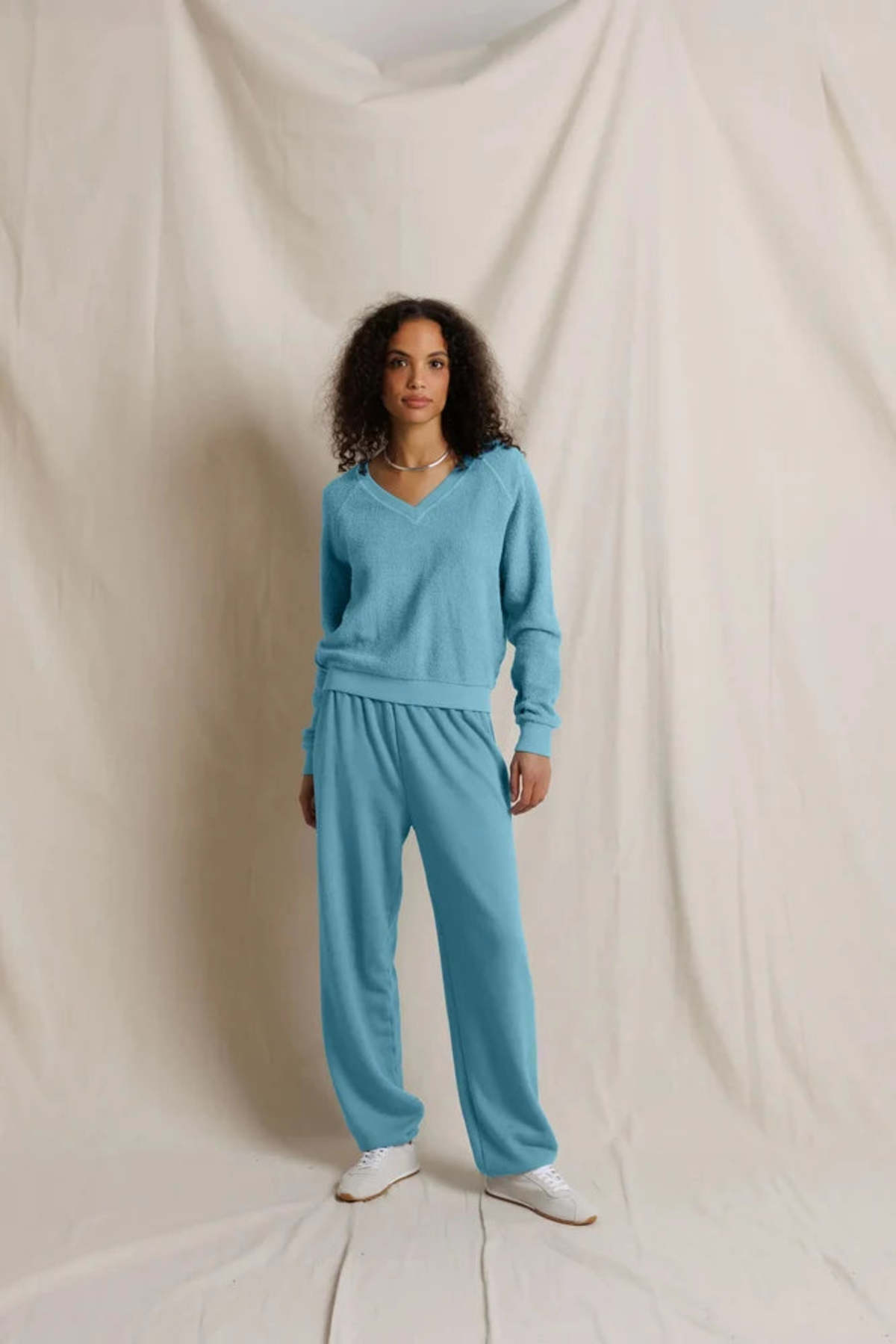 Woman wearing the Zuri Fleece V-neck sweatshirt in Milky Blue and matching sweatpants against a plain background.