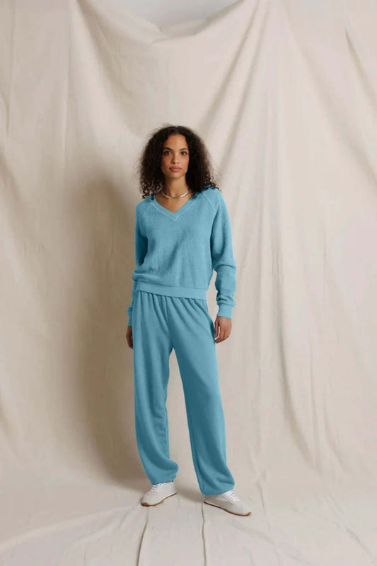 Woman wearing the Zuri Fleece V-neck sweatshirt in Milky Blue and matching sweatpants against a plain background.