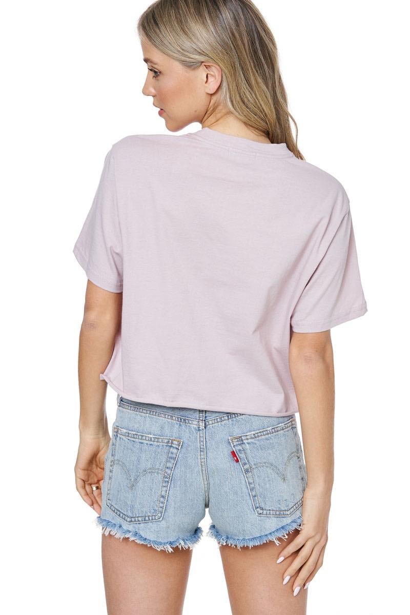 Back view of woman wearing a dusty rose t-shirt and denim shorts on a white background