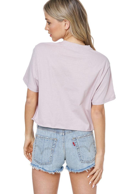 Back view of woman wearing a dusty rose t-shirt and denim shorts on a white background