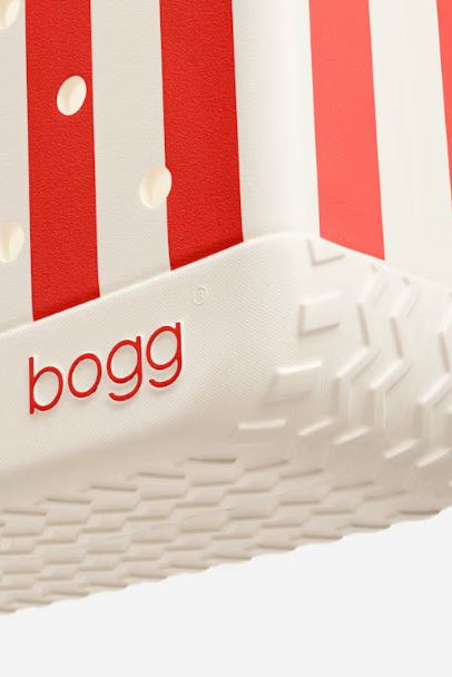 Close-up of a Bogg bottom showing the side with red and white vertical stripes, a white textured sole, and the red 'bogg' logo on the side.