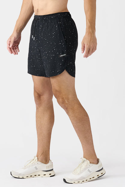 Side view of person wearing black shorts with white splatters on a white background