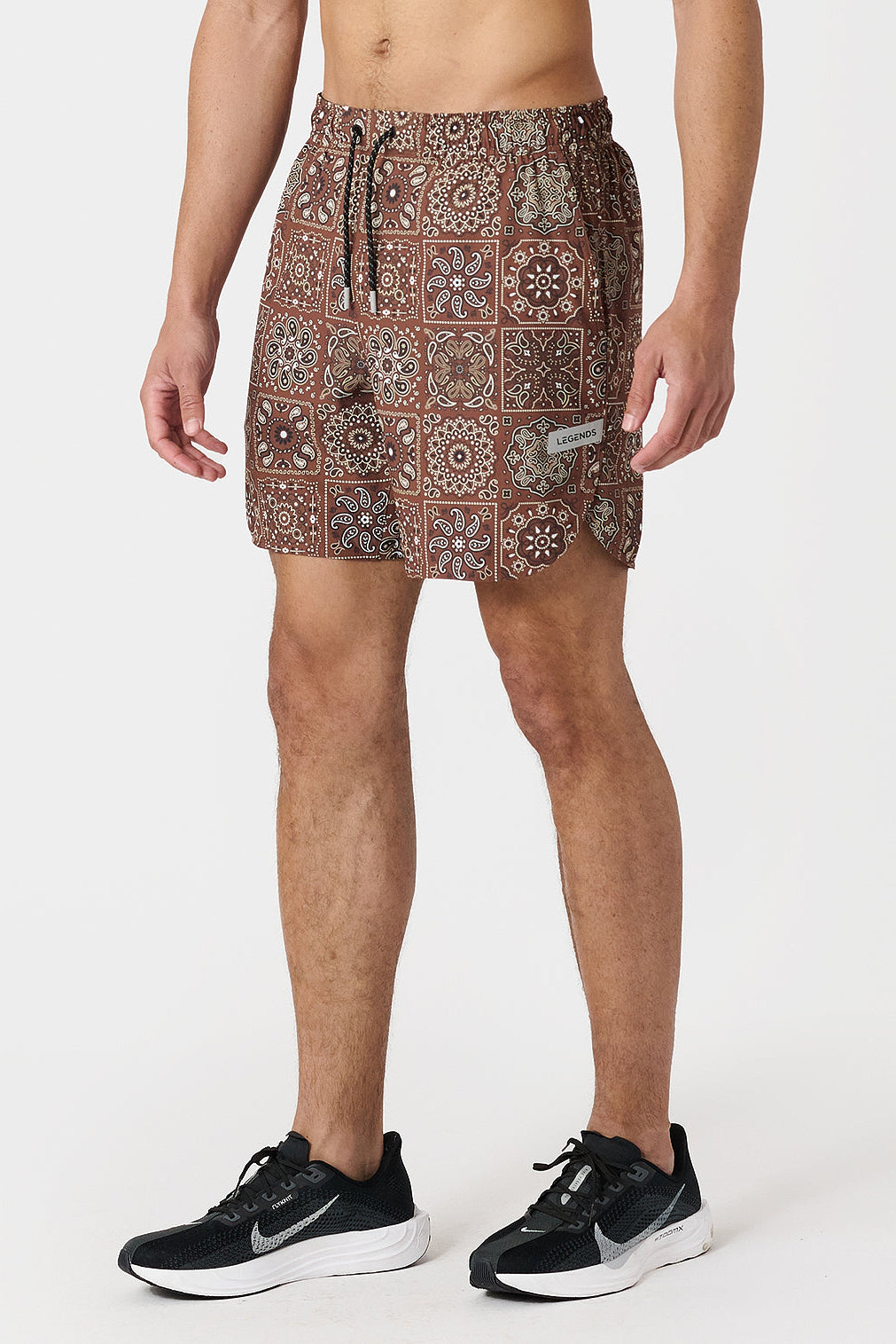 Person wearing copper paisley tile patterned shorts on a white background