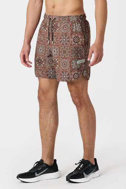 Person wearing copper paisley tile patterned shorts on a white background