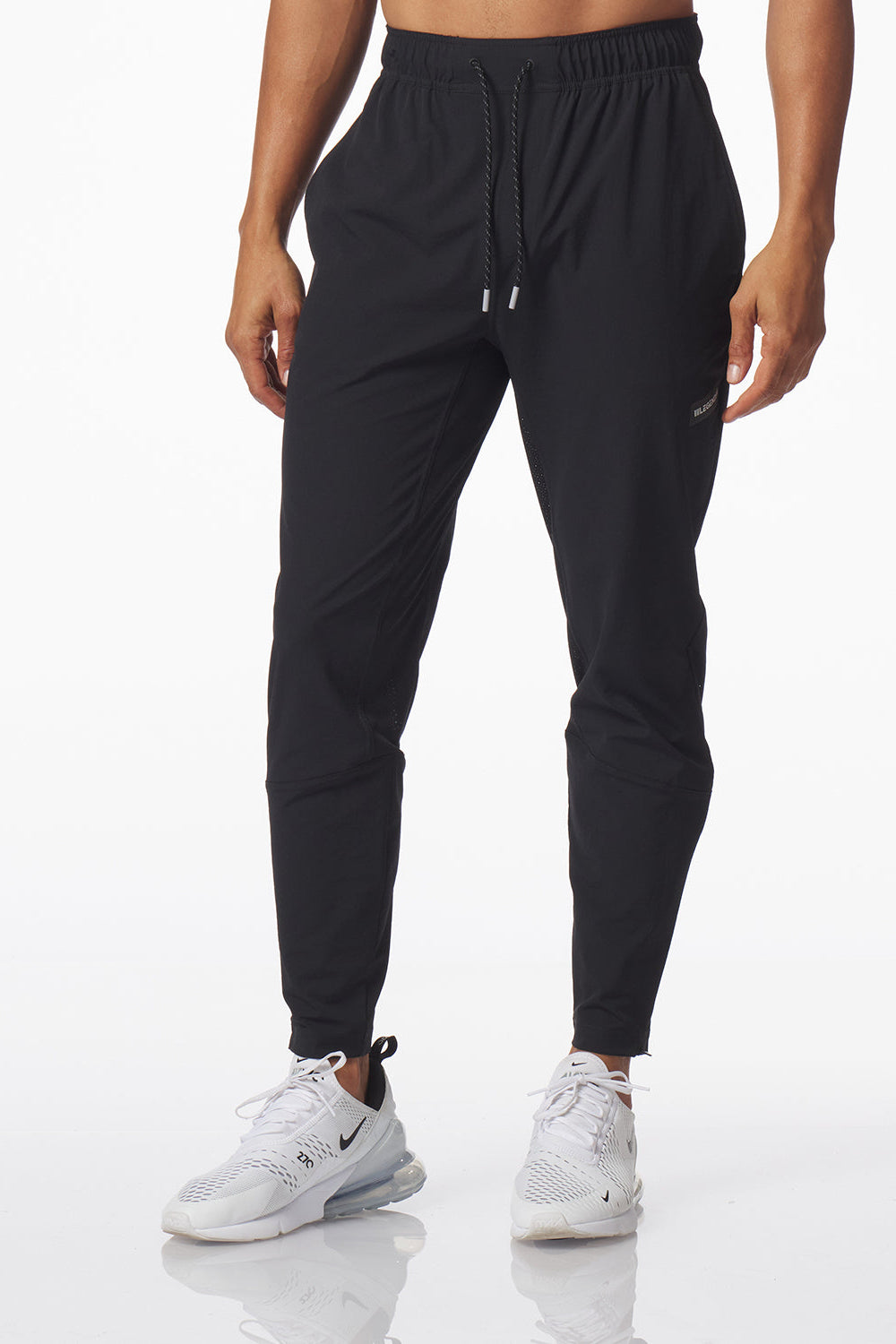 A person modeling black jogger-style carson athletic pants with a drawstring waist and elastic cuffs, paired with white sneakers, against a clean white studio background.