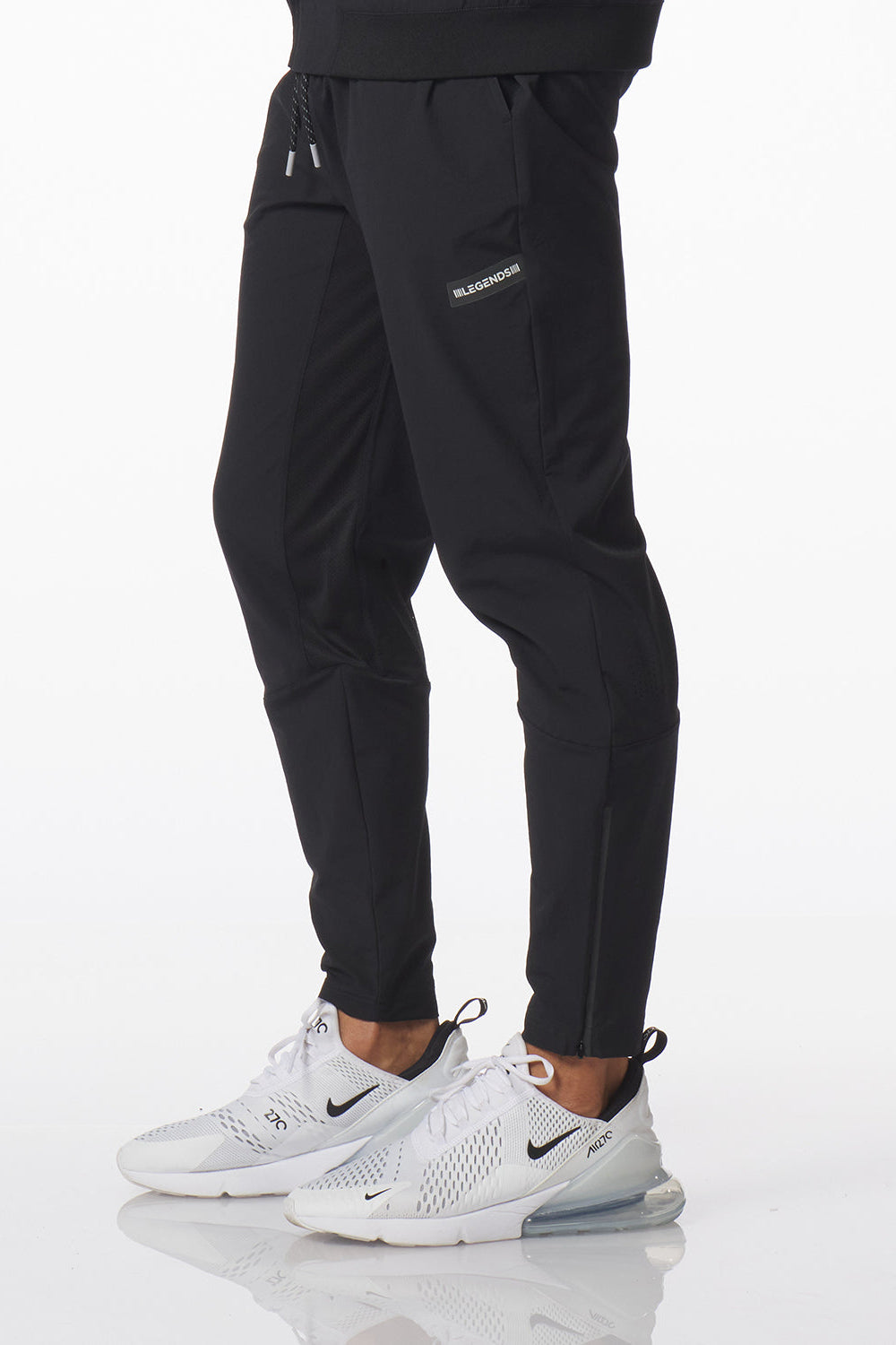 Black Carson athletic jogger pants with side cargo pockets and a small white logo on the upper left thigh, shown on a model wearing white Nike sneakers against a white studio background.
