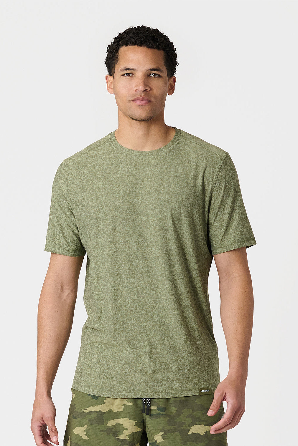 Man wearing a cypress heather green t-shirt and camouflage pants on a white background