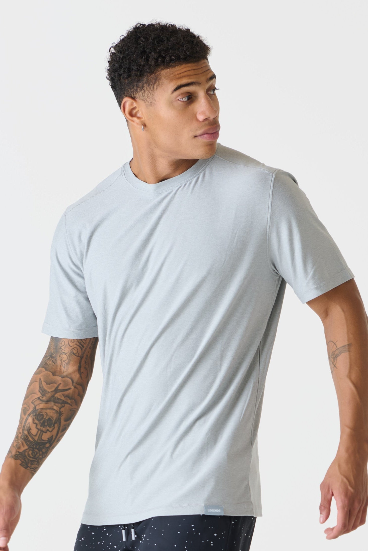 A man wearing a heather gray crew-neck t-shirt, shown from a three-quarters angle against a plain light gray studio background.