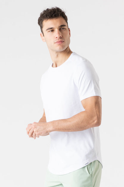 A man wearing a white short-sleeve crewneck t-shirt and light green pants, photographed against a clean white studio background.