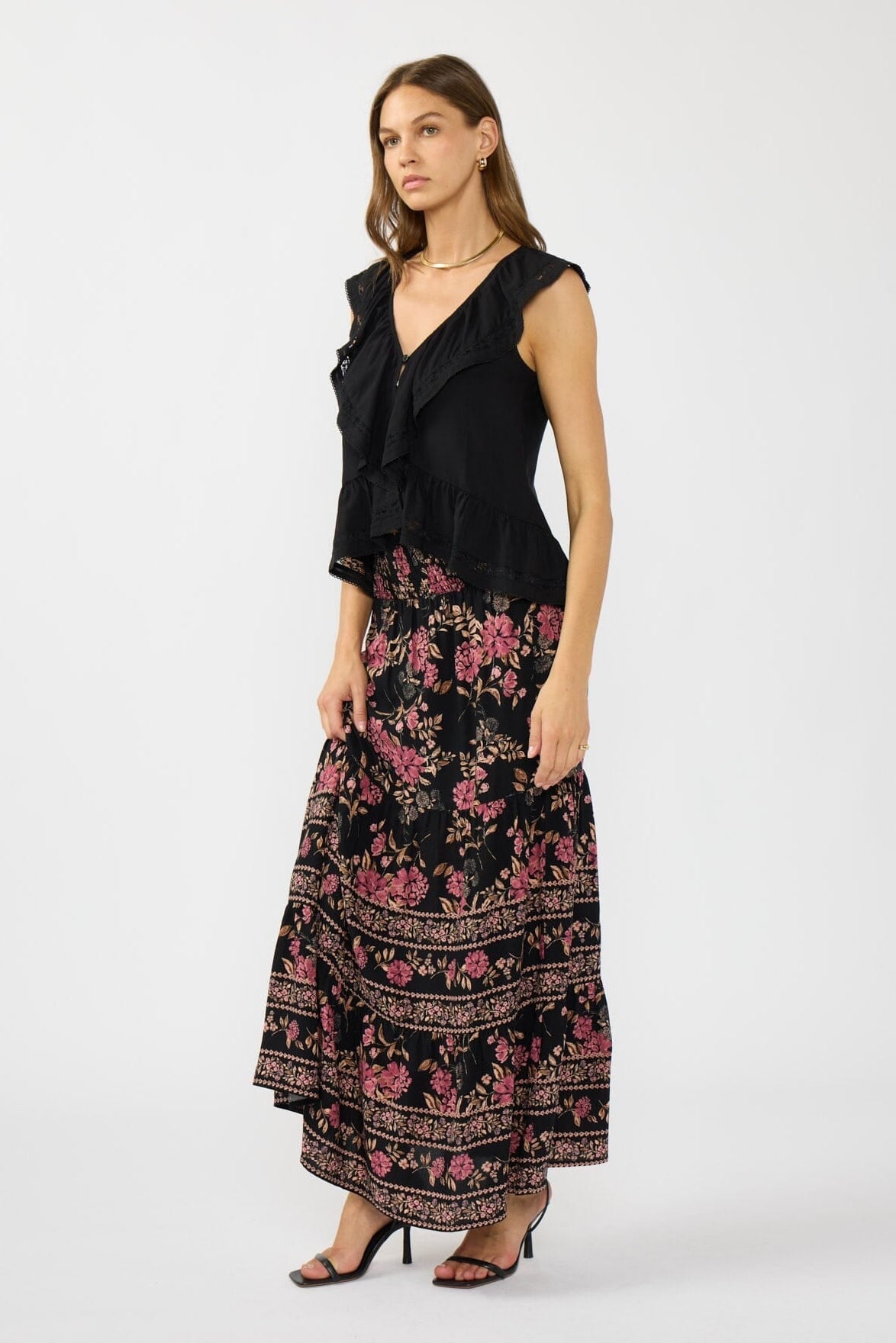 Woman wearing a black sleeveless ruffle top with floral pattern skirt on a white background