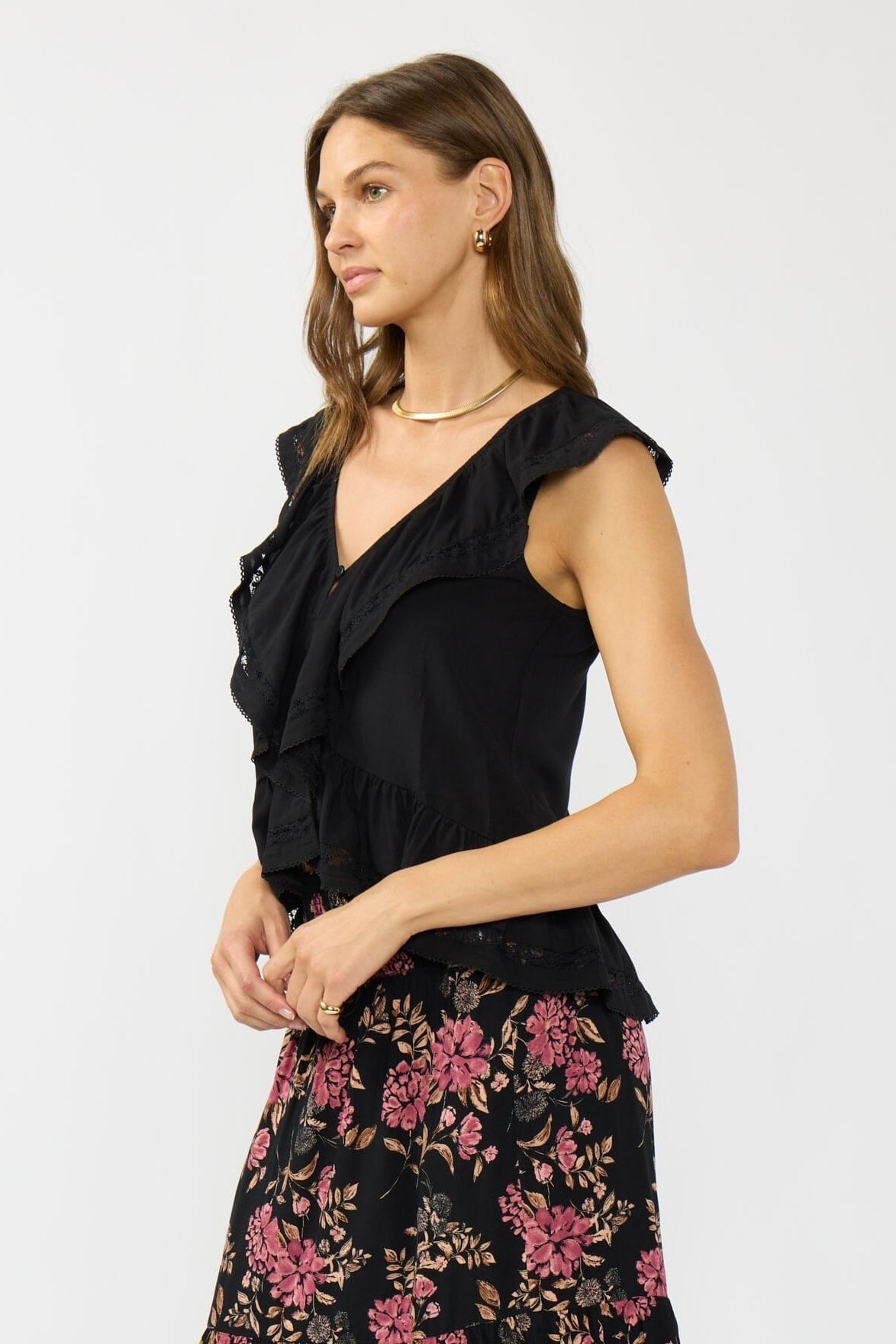 Side view of woman wearing a black sleeveless ruffle top with floral skirt on a white background
