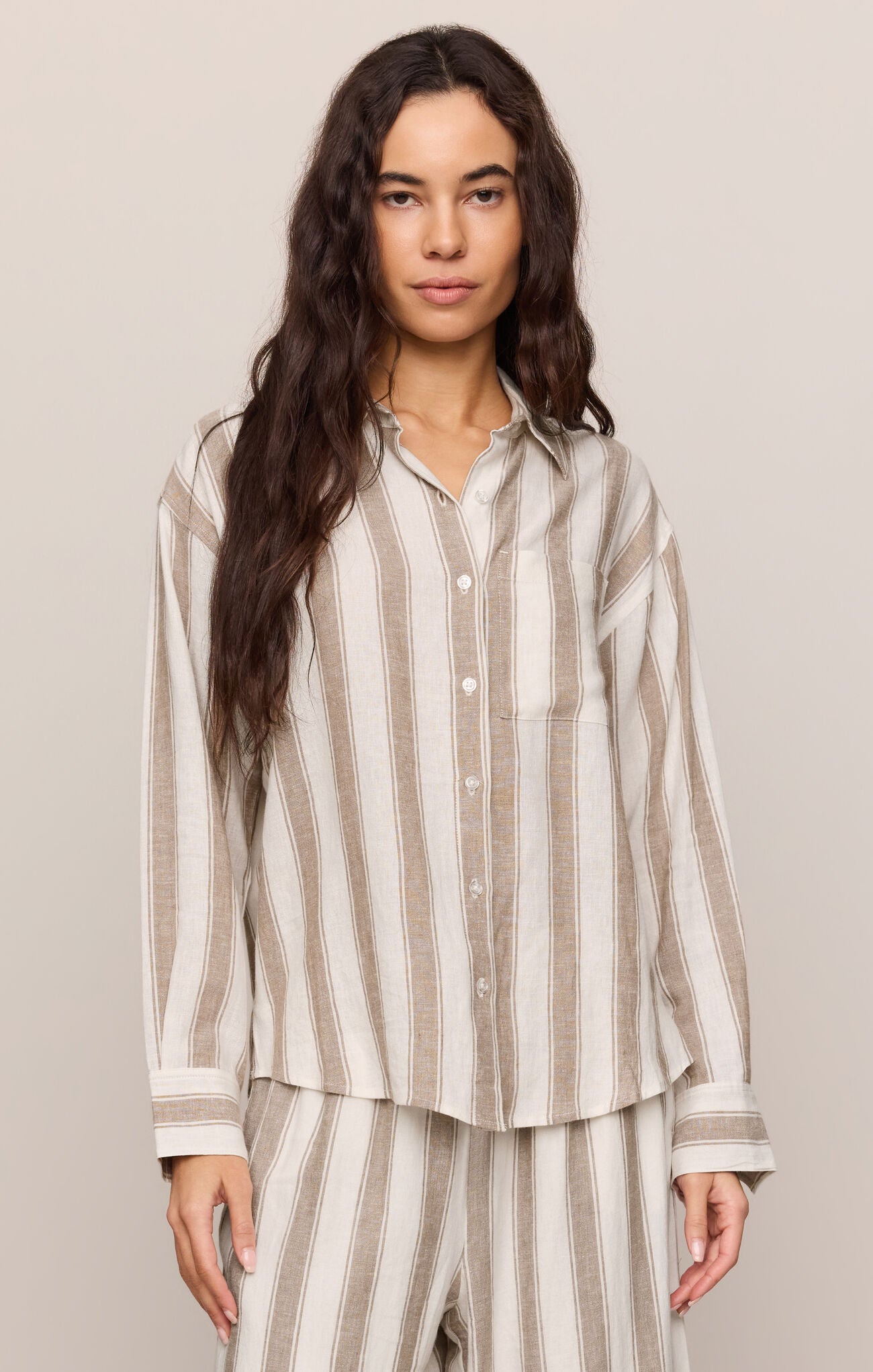 Woman wearing a light toffee striped button up top and matching pants 