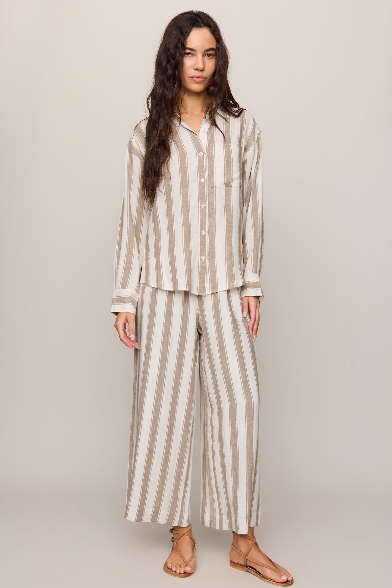 Woman wearing a light toffee striped button up top and matching pants against a plain background