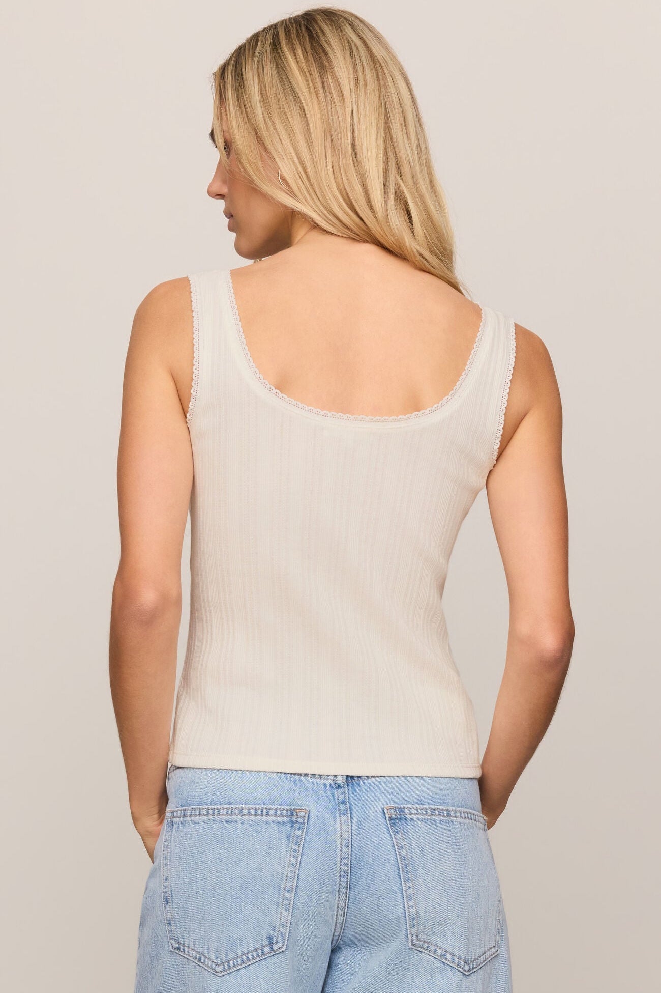 Back view of woman wearing a cloud color tank top and light blue jeans against a plain background