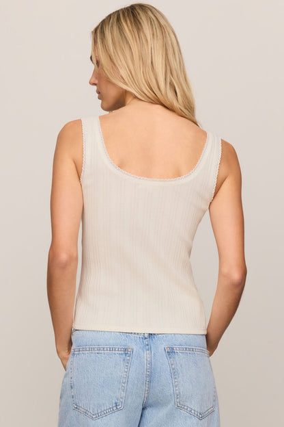 Back view of woman wearing a cloud color tank top and light blue jeans against a plain background