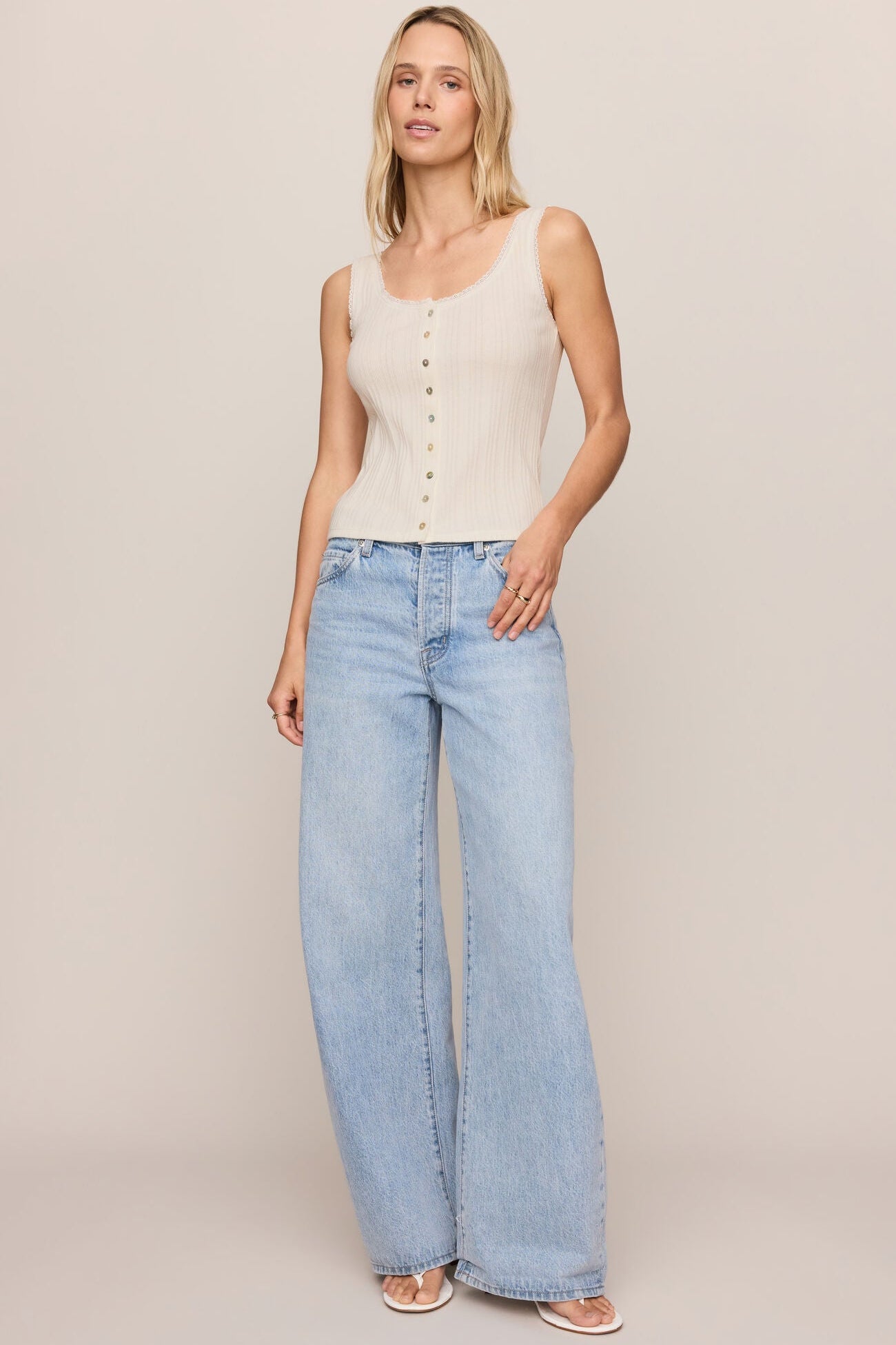 Woman wearing a cloud color sleeveless top and light blue jeans on a plain background