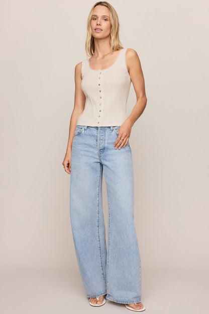 Woman wearing a cloud color sleeveless top and light blue jeans on a plain background