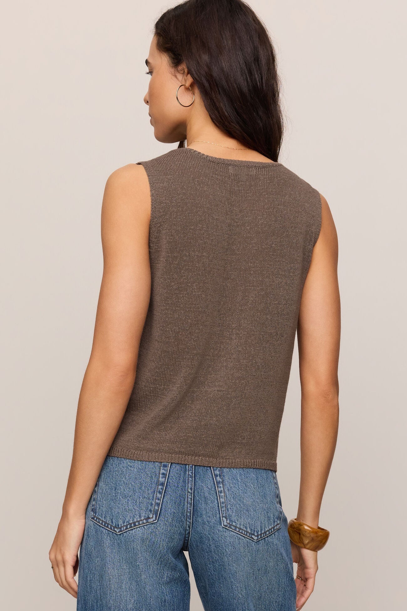 Woman wearing a pebble coast brown sleeveless top and blue jeans on a beige background