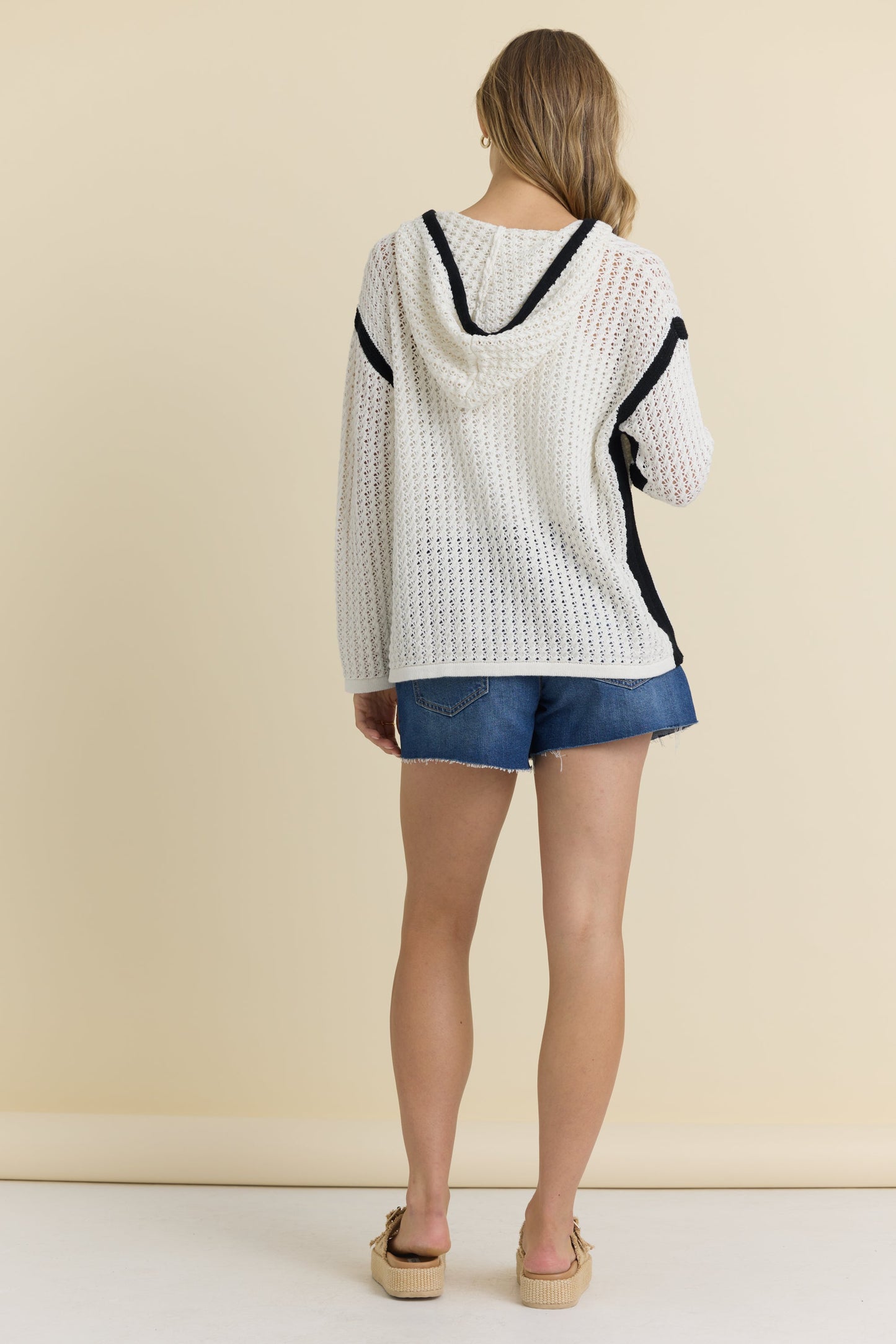 Back view of woman wearing an ivory crochet hooded sweater with black detailing 