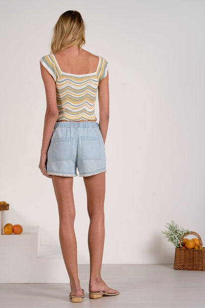 Woman wearing a striped top and light blue denim fray shorts standing in a minimalistic room.
