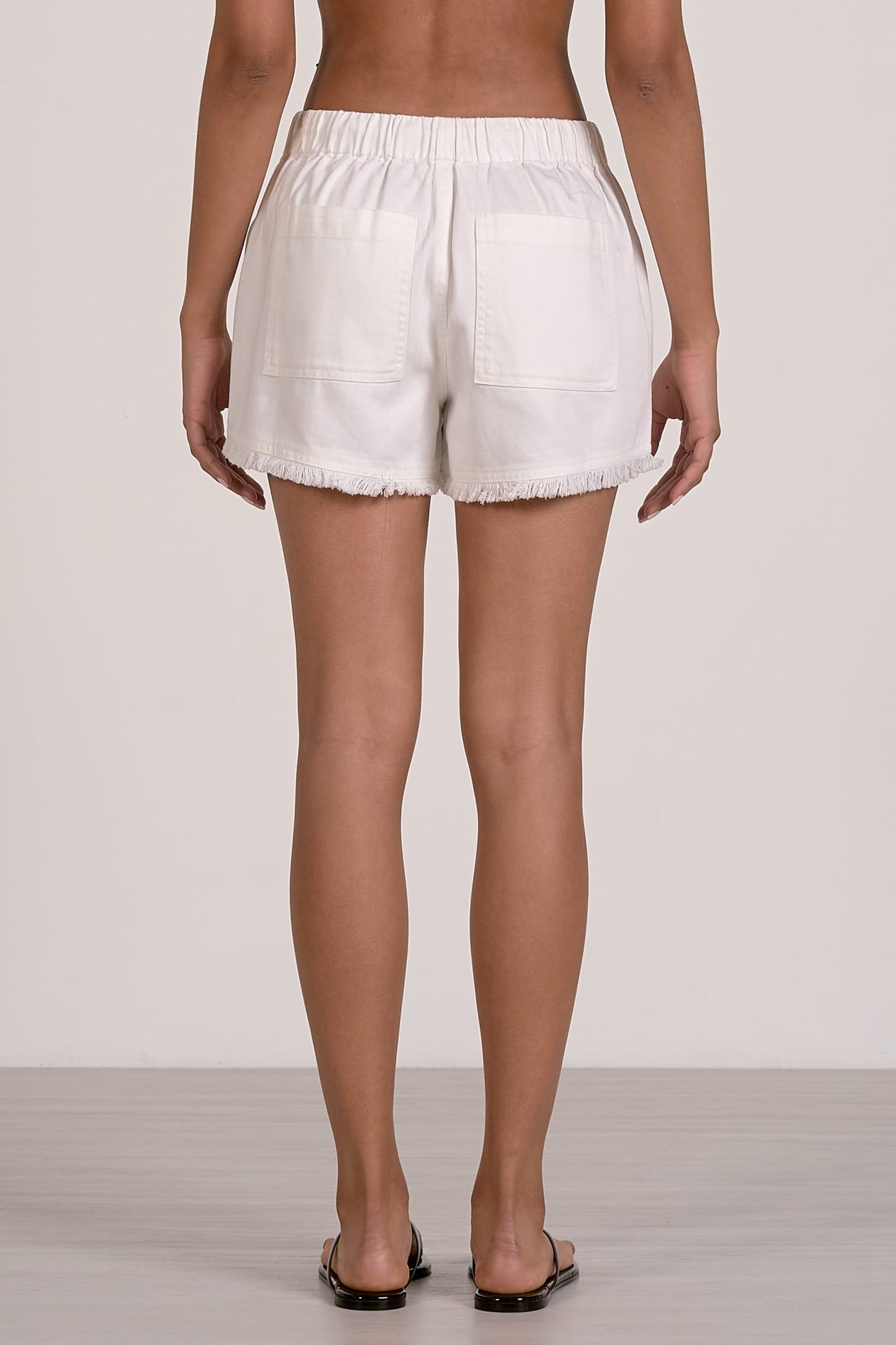 Back view of white fray shorts worn by a person on a plain background