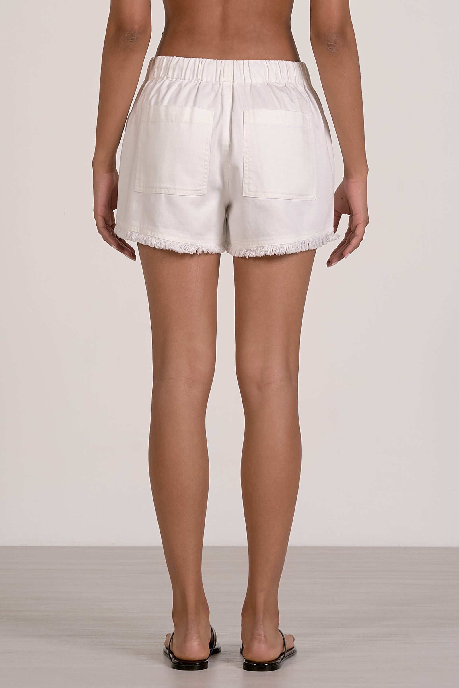 Back view of white fray shorts worn by a person on a plain background