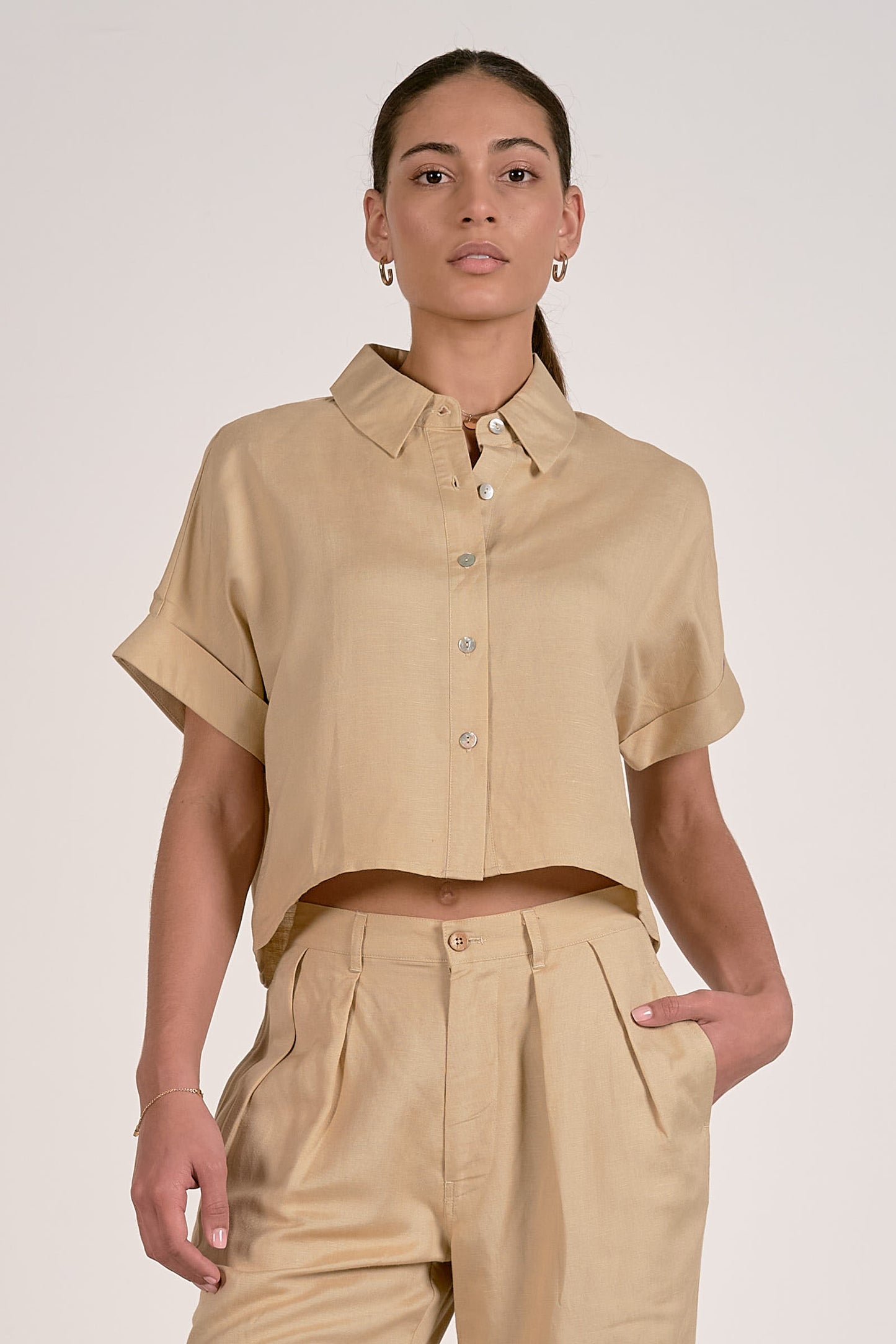 Person wearing an oatmeal short-sleeve button up shirt and pants on a plain background